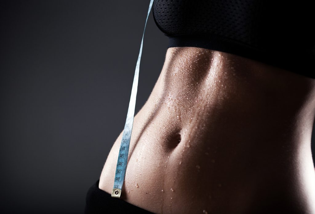 Woman sporty belly after exercise with measuring tape