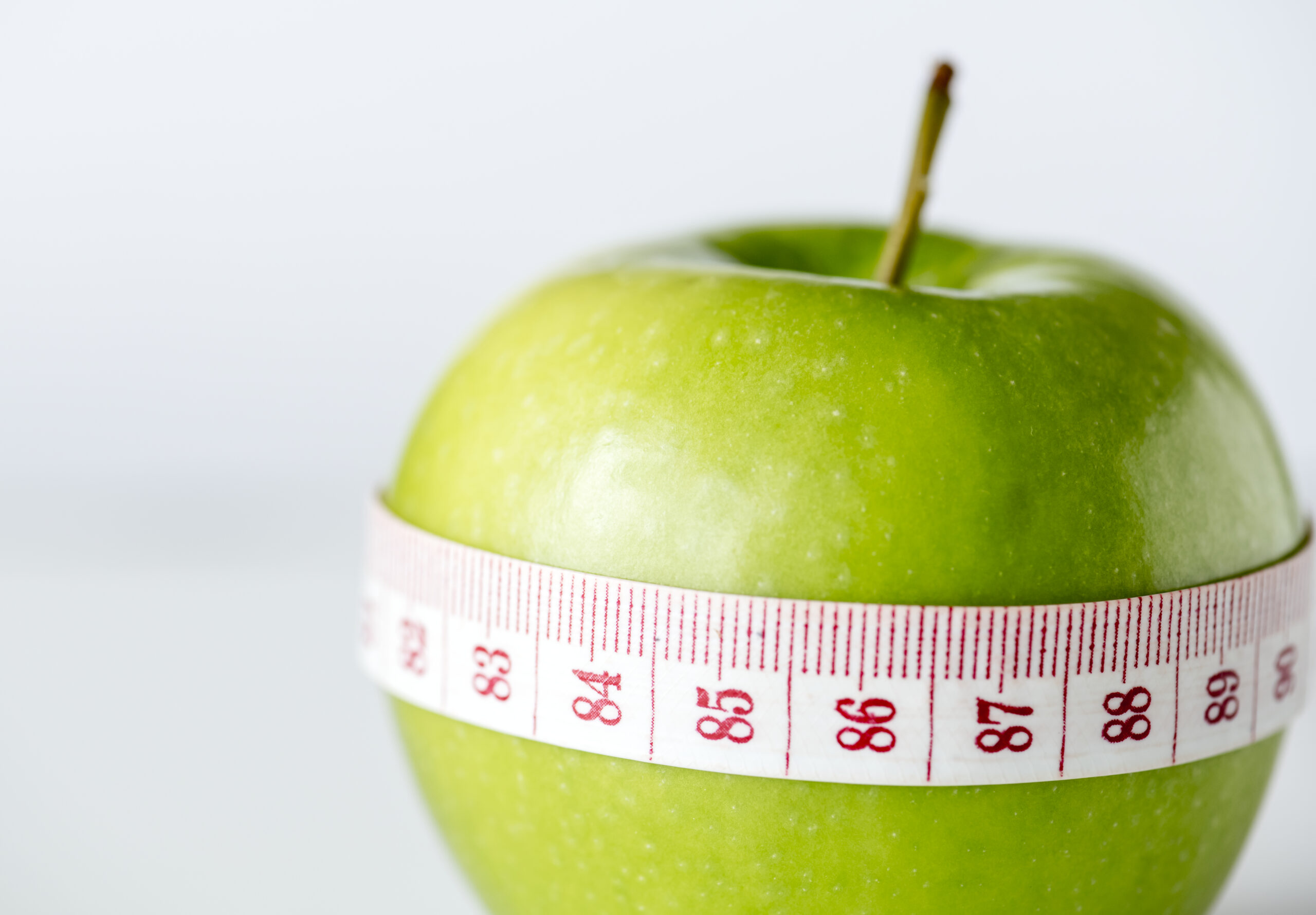 Green apple with a tape measure wrapped around it, representing semaglutide for weight loss
